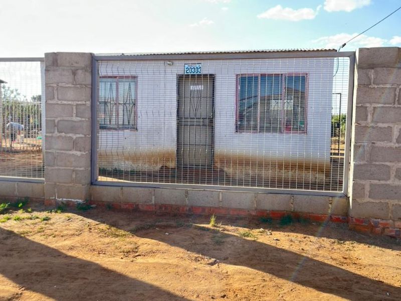 Front view of a single-story house featuring security fencing, metal security gate, and window bars, with visible exterior wall maintenance required.