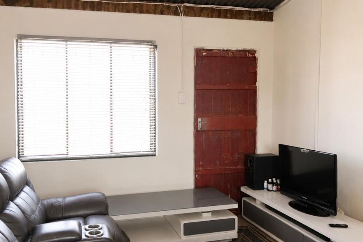 A living room featuring a corrugated iron ceiling, exposed timber beams, and a window with venetian blinds.