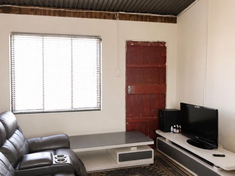 A living room featuring a corrugated iron ceiling, exposed timber beams, and a window with venetian blinds.