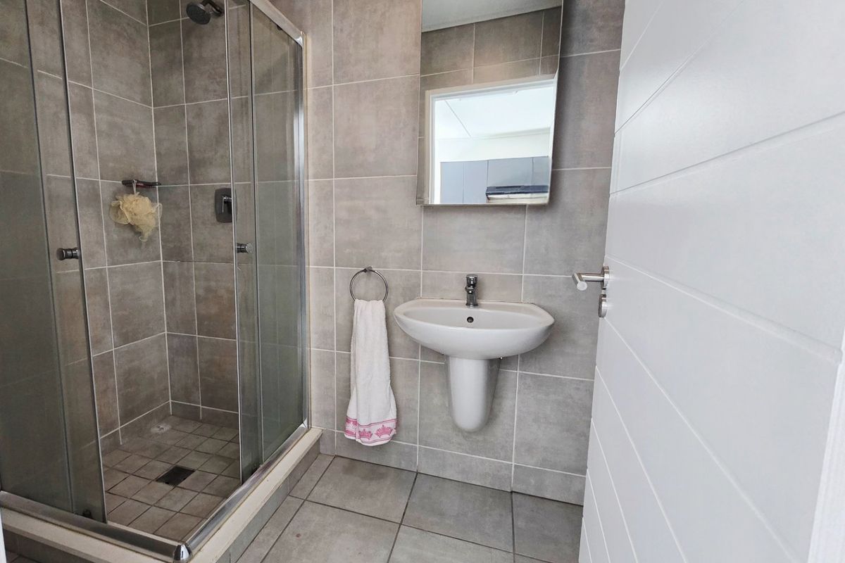 A modern bathroom featuring a glass-enclosed shower, pedestal washbasin, and neutral grey wall and floor tiles.