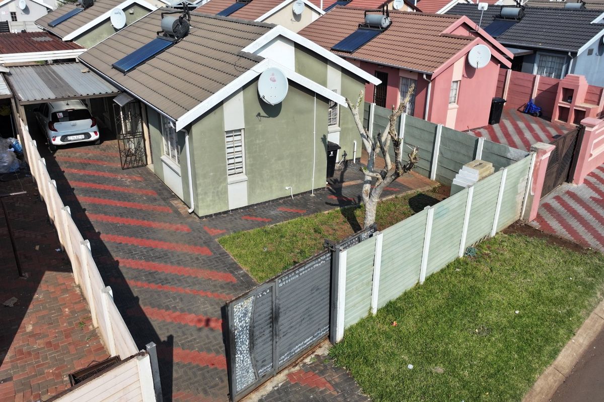 Aerial view of a residential property featuring a tiled roof with solar water heating, a paved driveway, and perimeter precast concrete walling.