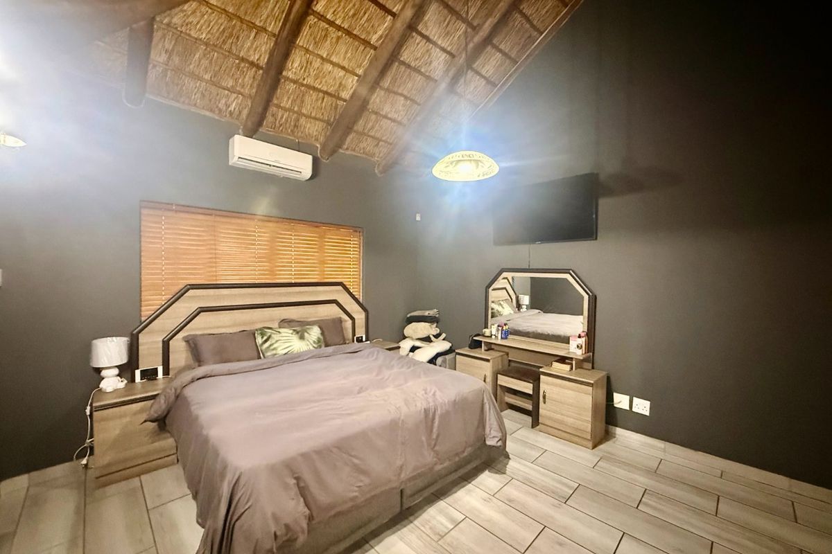 Spacious bedroom featuring a high vaulted thatched ceiling with exposed timber rafters, tiled flooring, and a wall-mounted air conditioning unit.