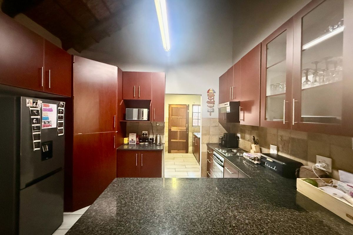 A functional kitchen featuring dark wood cabinetry, granite countertops, tiled backsplash, and exposed timber ceiling beams, with an adjacent scullery area.