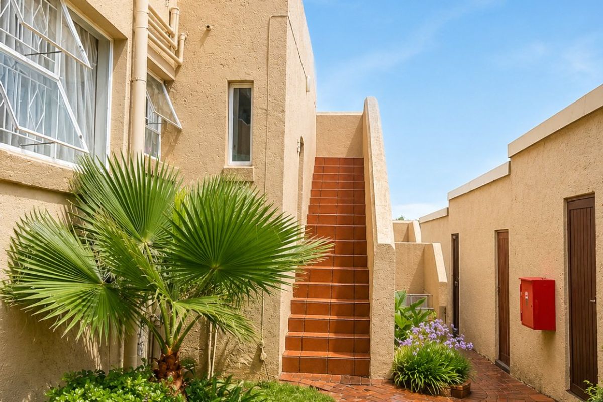 Exterior view of an apartment complex featuring a brick pathway, landscaped garden, and an external staircase leading to upper levels.