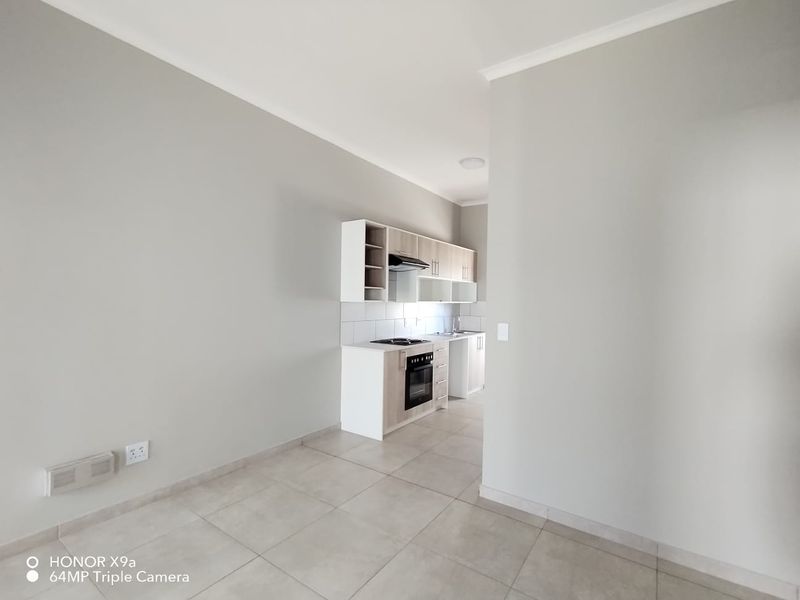 A clean, modern kitchen area featuring built-in cabinetry, an electric oven and hob, and tiled flooring in an open-plan layout.