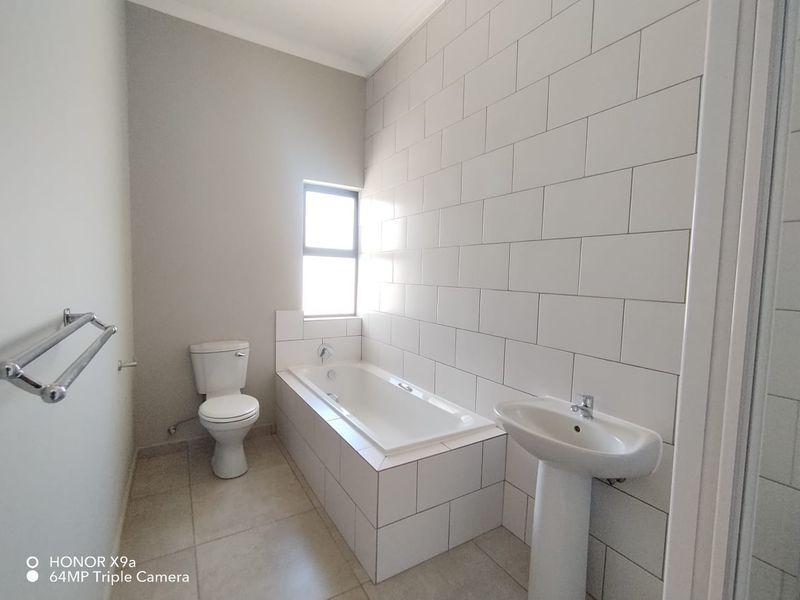 A clean, modern bathroom featuring a built-in bathtub, pedestal basin, and toilet with neutral wall tiling and floor tiles.