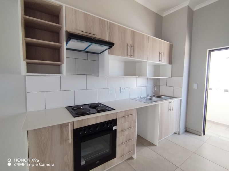 Modern kitchen featuring light wood-finish cabinetry, built-in oven and hob, extractor fan, and a clean tiled backsplash.