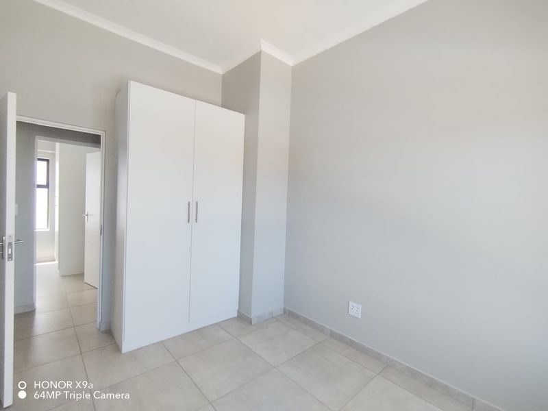 A clean, empty bedroom featuring neutral tiled flooring, a built-in white wardrobe, and simple cornice detailing.