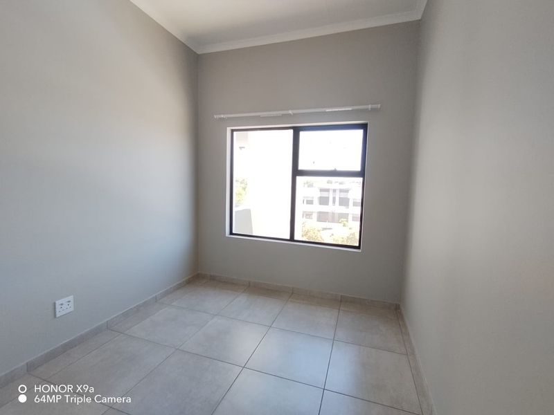 A clean, empty bedroom featuring neutral wall paint, large aluminium-framed window, and modern tiled flooring, ready for personalization.
