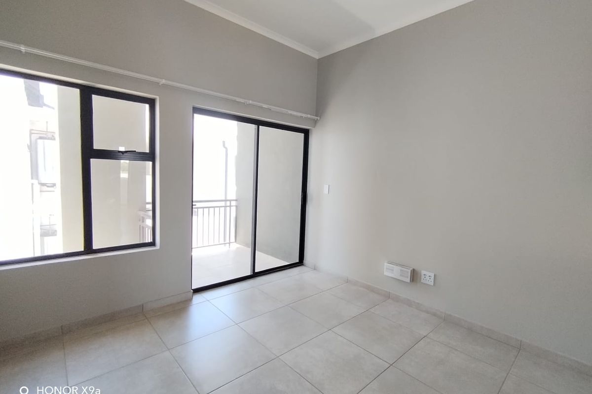 A bright, empty living area featuring neutral tiled flooring, large aluminium-framed windows, and a sliding glass door leading to an outdoor space.