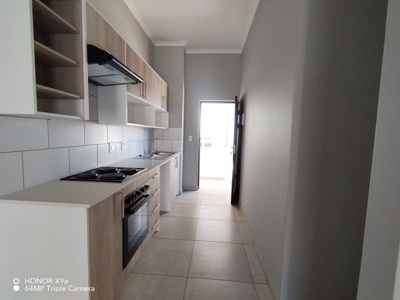 A modern, clean-lined kitchen featuring light wood-tone cabinetry, built-in oven and hob, tiled splashbacks, and direct access to an outdoor area.