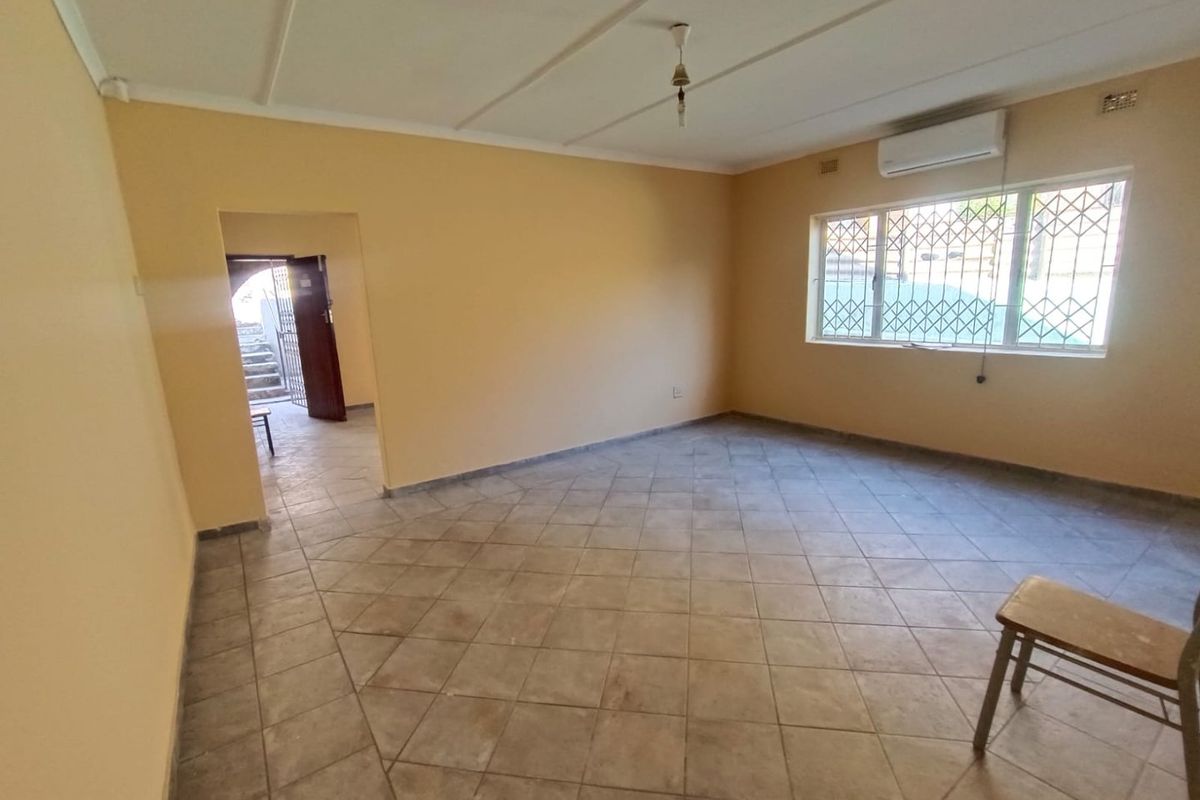 An empty living room featuring tiled flooring, a wall-mounted air conditioning unit, and security bars on the windows.