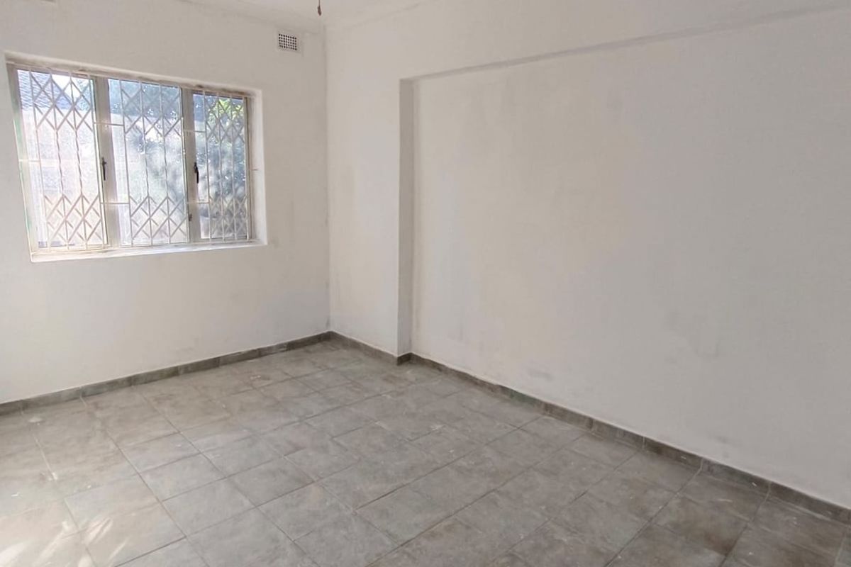 An empty bedroom featuring tiled flooring, a window with a security gate, and neutral walls, ready for renovation or staging.