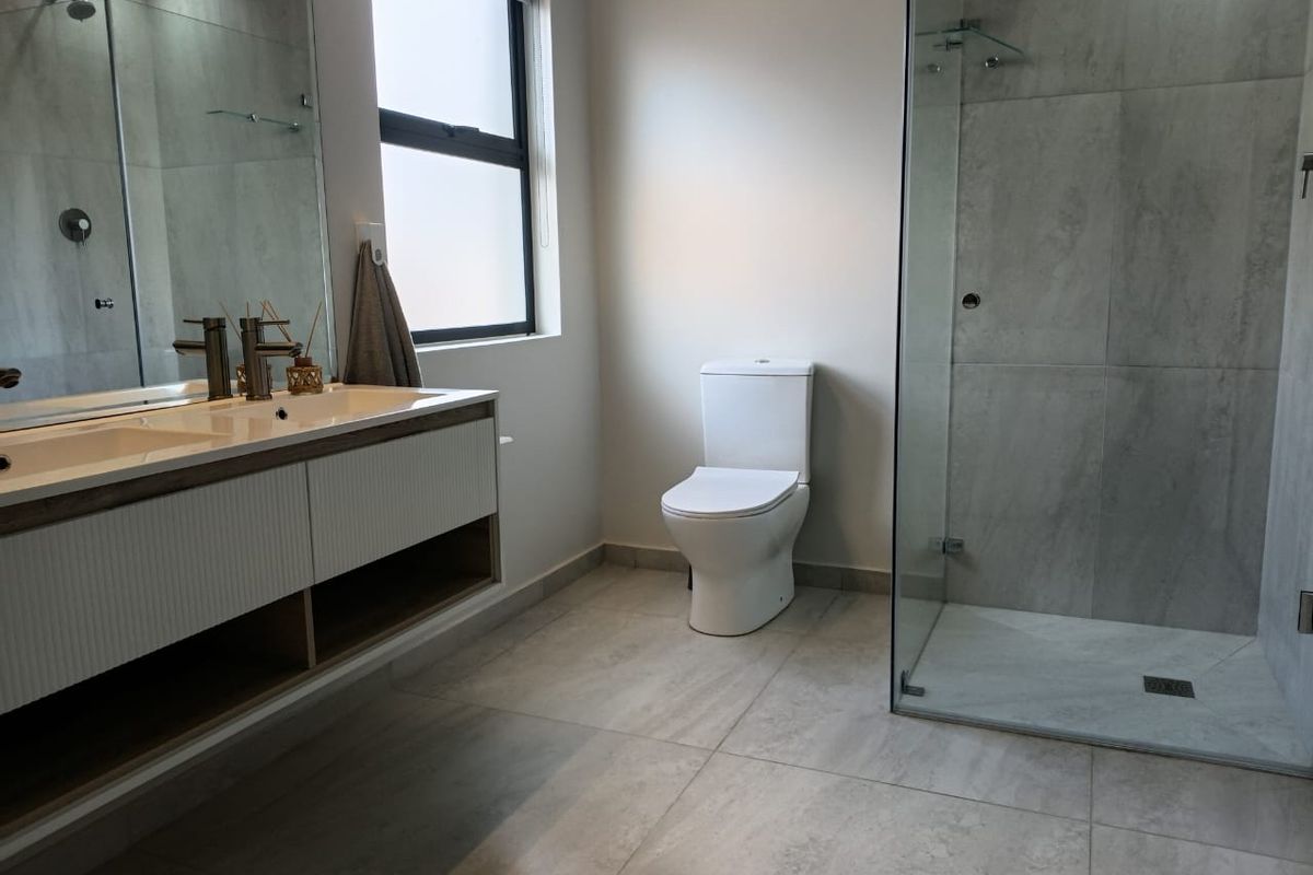 Modern bathroom featuring a double vanity with wall-mounted cabinetry, a spacious glass-enclosed shower, and neutral large-format floor tiles.