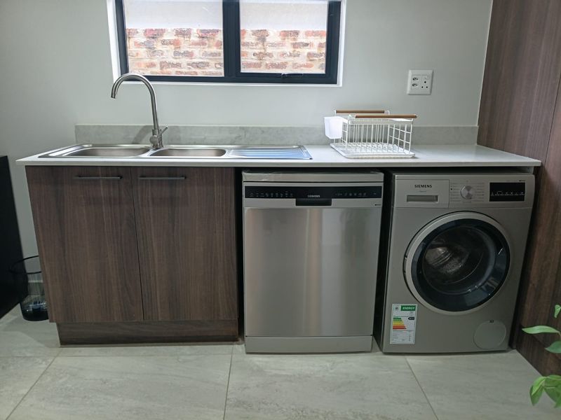 A modern, well-maintained laundry area featuring built-in cabinetry, a stainless steel sink, and integrated appliances including a dishwasher and washing machine.