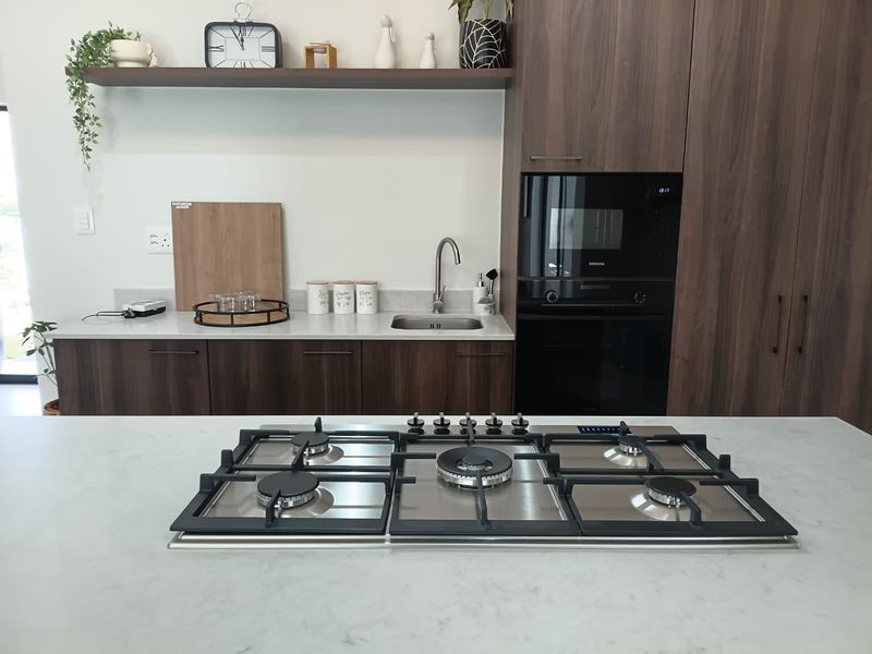 Modern kitchen featuring a central gas cooktop, integrated oven and microwave, stone countertops, and dark wood-grain cabinetry with a sleek undermount sink.