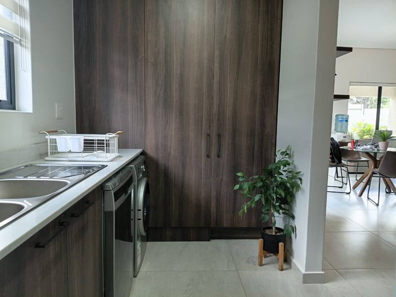 A functional laundry area featuring modern dark wood cabinetry, a stainless steel sink, and tiled flooring, providing efficient storage and utility space.