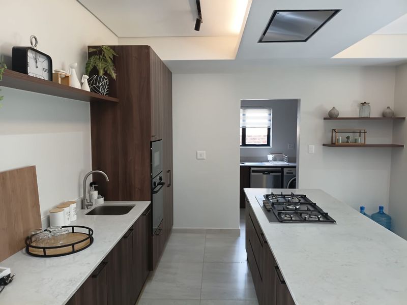 Modern kitchen featuring a central island with gas hob, stone countertops, dark wood cabinetry, and an adjacent scullery area.