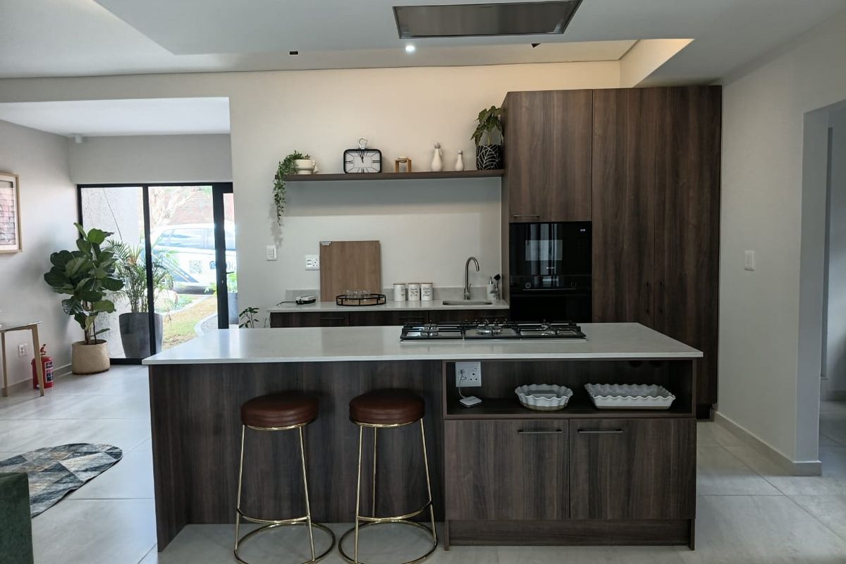 Modern kitchen featuring a central island with a gas hob, stone countertops, dark wood cabinetry, and integrated appliances in an open-plan layout.