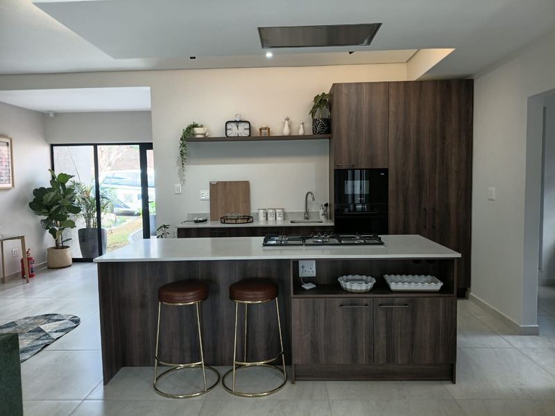 Modern kitchen featuring a central island with a gas hob, stone countertops, dark wood cabinetry, and integrated appliances in an open-plan layout.