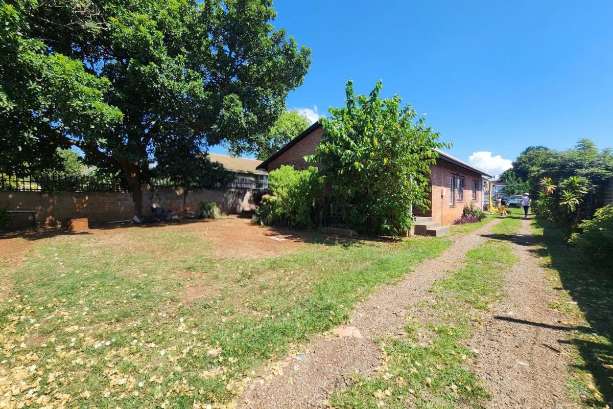 Rear view of the brick house featuring a gravel driveway, established garden area, and boundary walling.