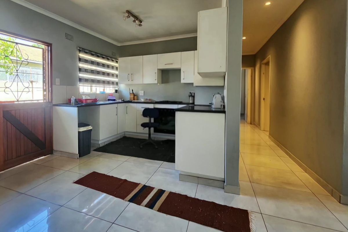 A functional kitchen featuring white built-in cabinetry, dark countertops, built-in oven and hob, and tiled flooring, with direct access to an exterior door.