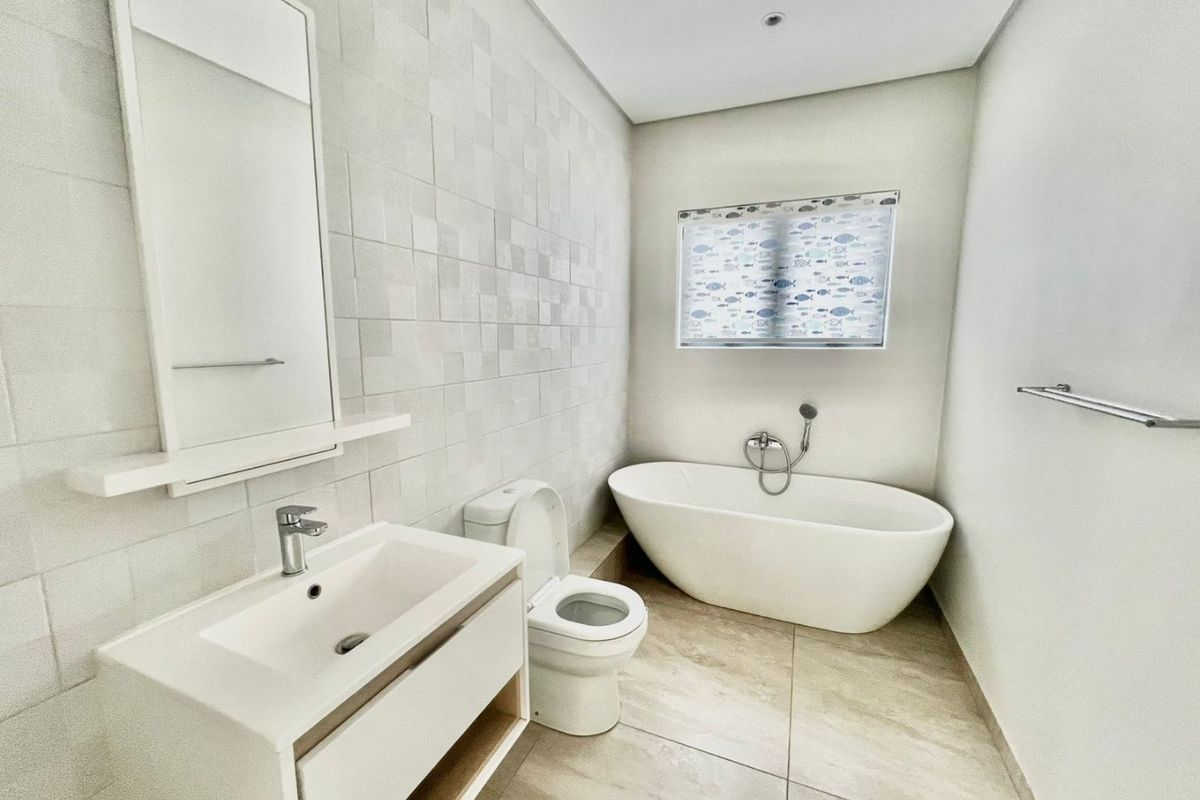 Modern bathroom featuring a sleek freestanding bathtub, contemporary vanity with basin, toilet, and neutral floor-to-ceiling tiling.