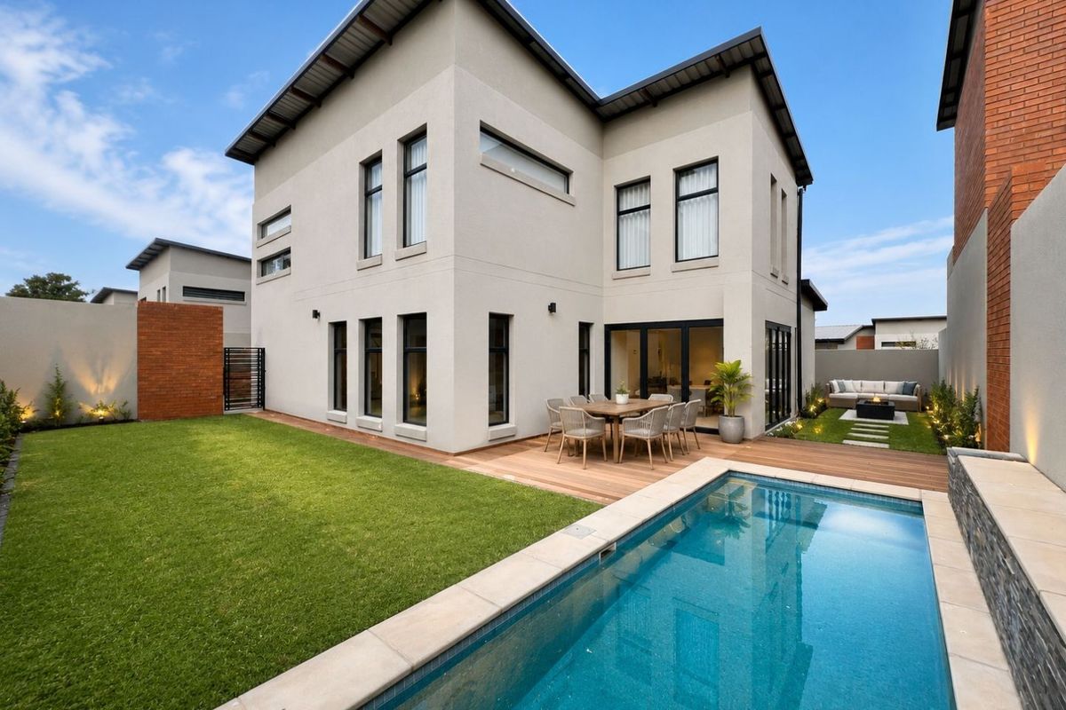 A well-maintained rear exterior featuring a swimming pool, timber decking, landscaped lawn, and modern architectural facade with large glass sliding doors.
