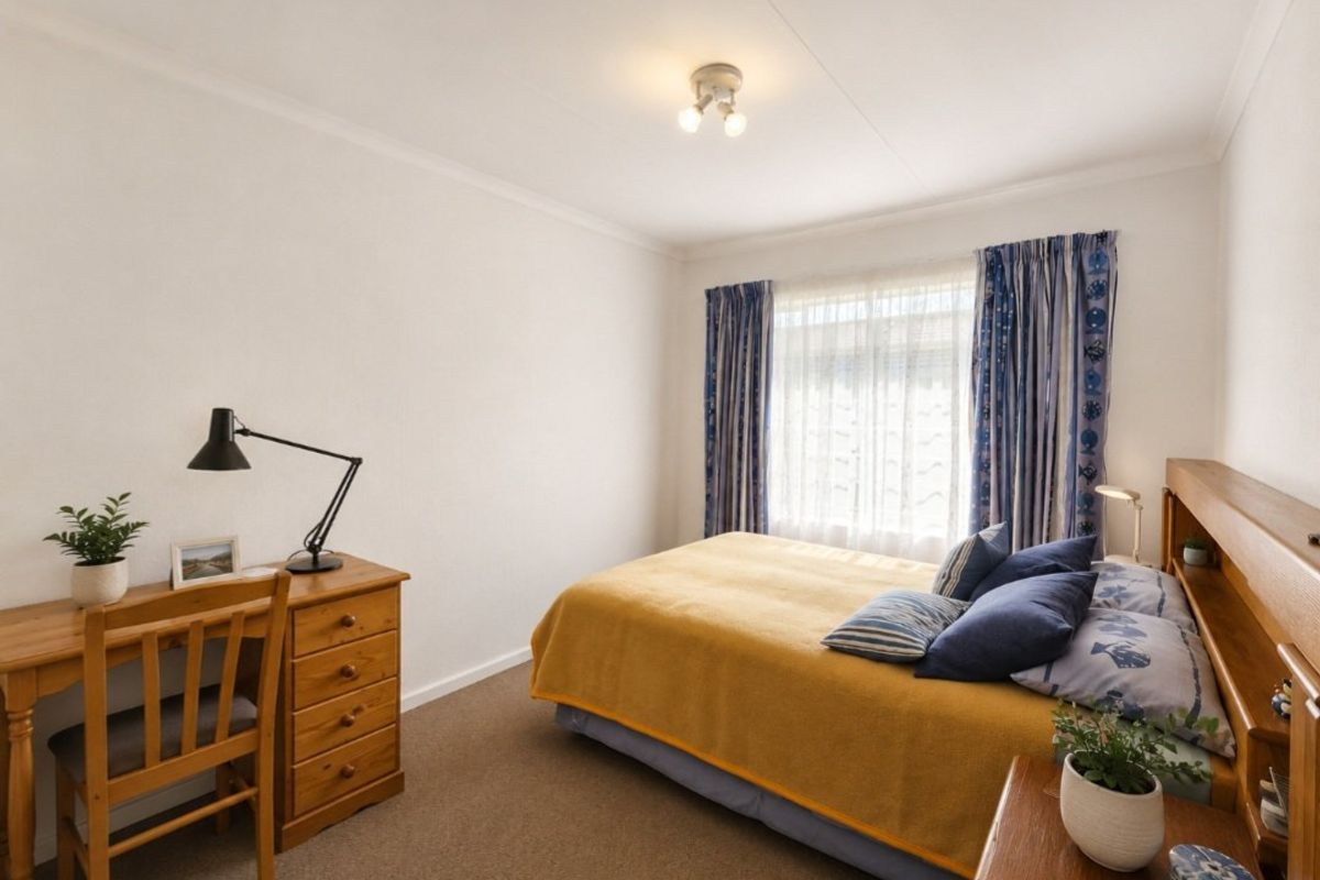 A well-lit bedroom featuring neutral wall finishes, carpeted flooring, and a large window with curtains.
