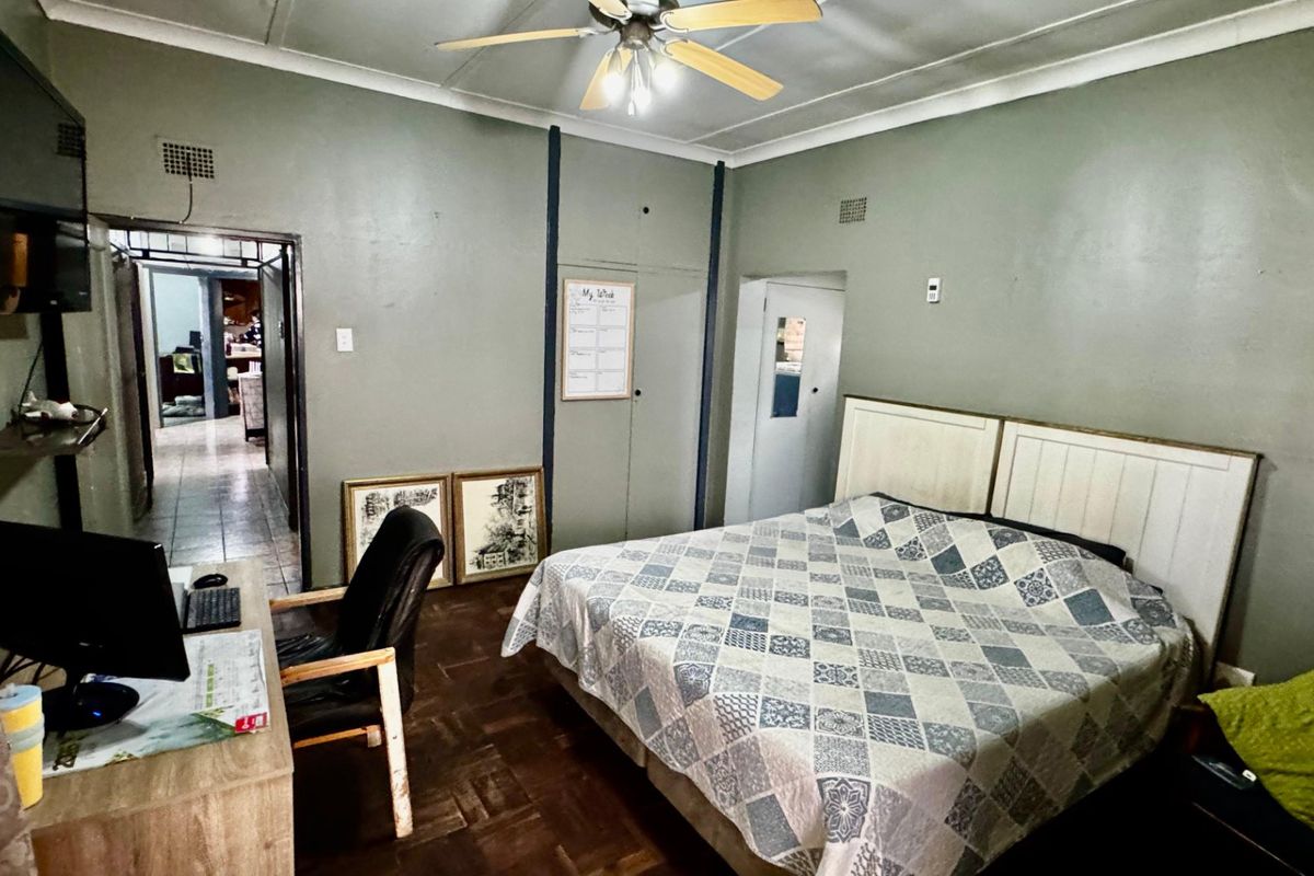 A bedroom featuring parquet flooring, built-in cupboards, and a ceiling fan, offering a functional space with potential for cosmetic updates.