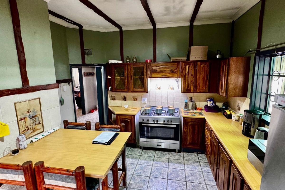 A dated kitchen featuring wooden cabinetry, a gas stove, tiled splashbacks, and exposed ceiling beams, offering potential for a modern renovation.