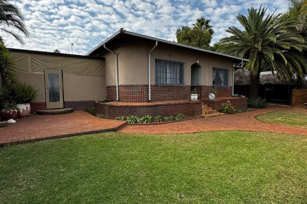 Rear view of the house featuring a brick facade, security bars on windows, and a paved patio area leading onto a well-maintained lawn.