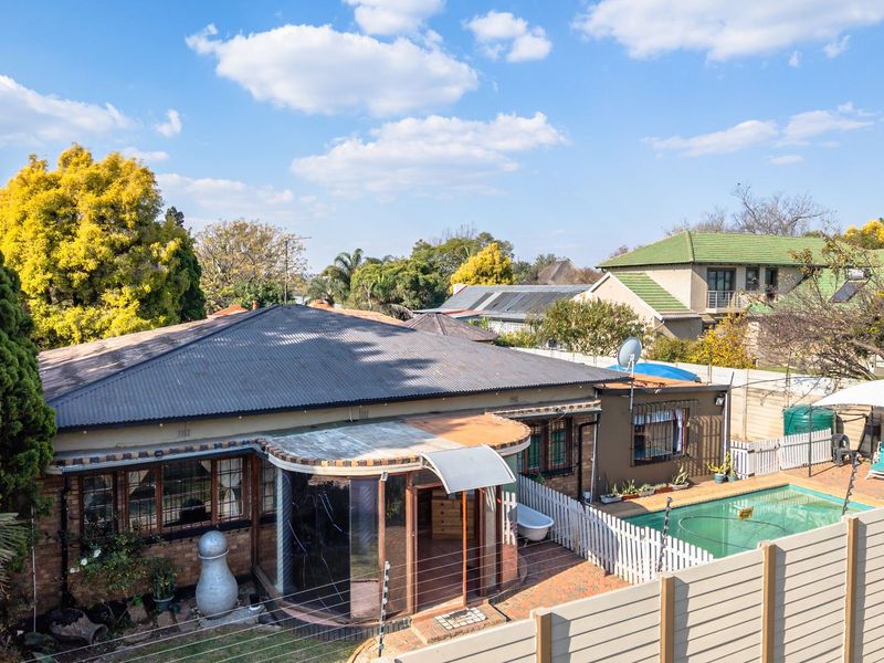 Aerial view of the rear property featuring a swimming pool, paved patio area, and a distinctive curved glass enclosure against a brick facade.