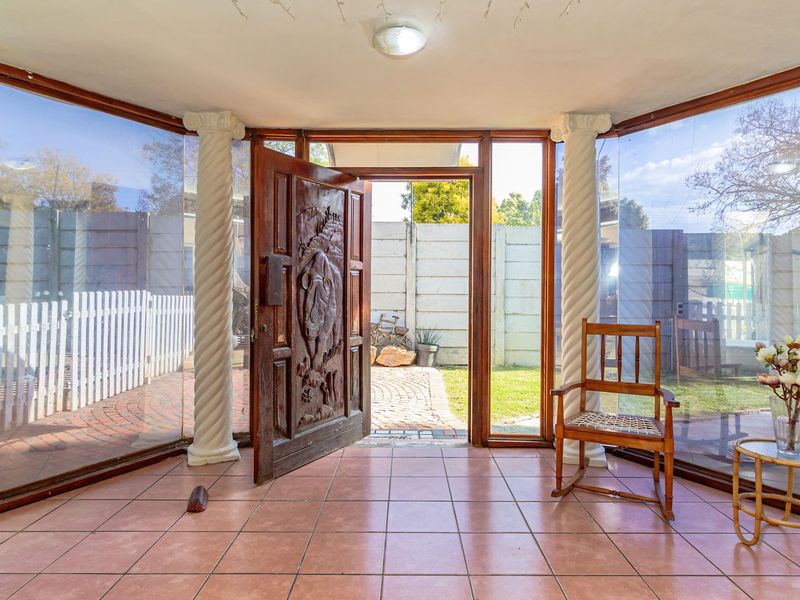 An entrance foyer featuring large glass panels, decorative columns, and a unique carved wooden front door opening to a paved outdoor area.