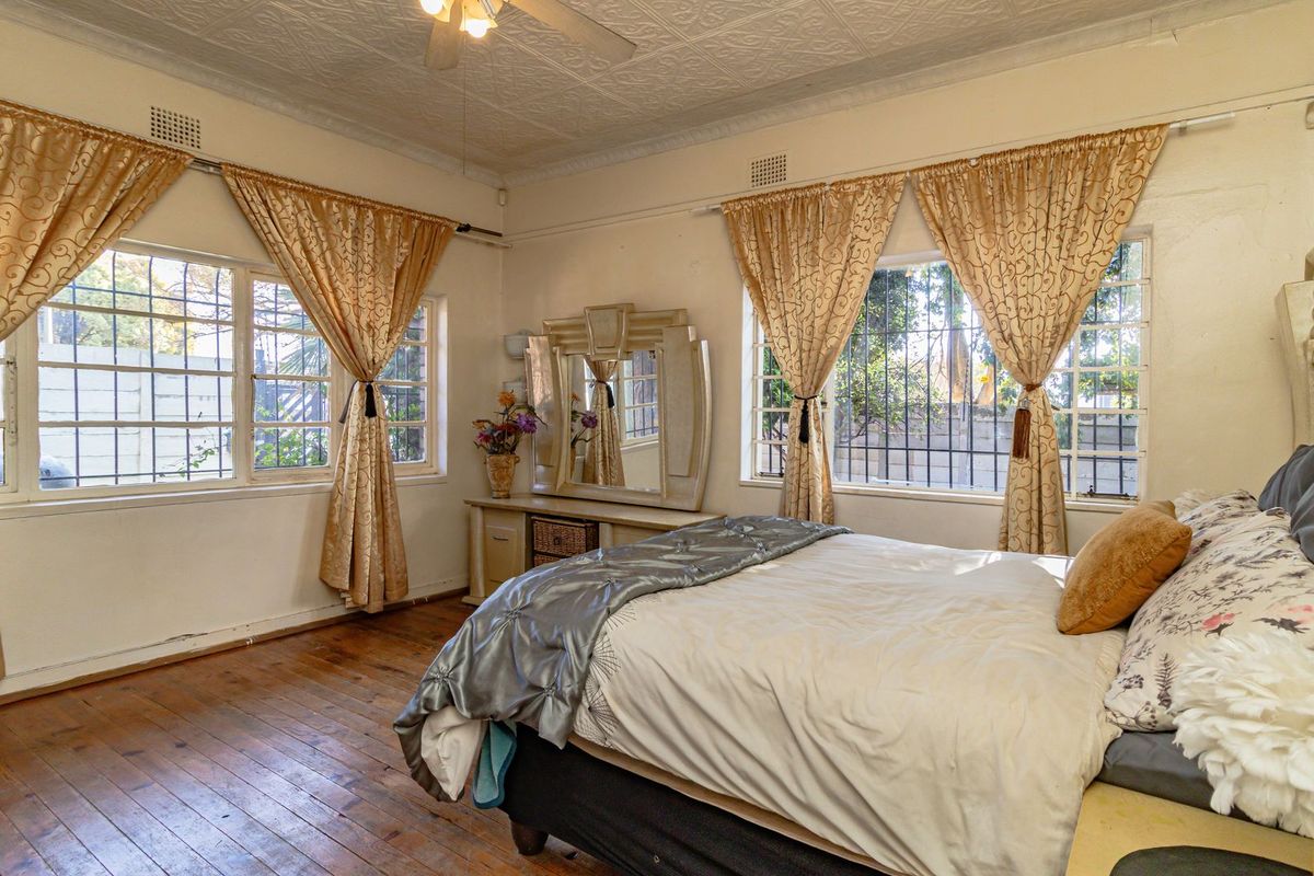 Spacious bedroom featuring original pressed metal ceilings, timber flooring, and large windows with security bars, offering a classic character aesthetic.