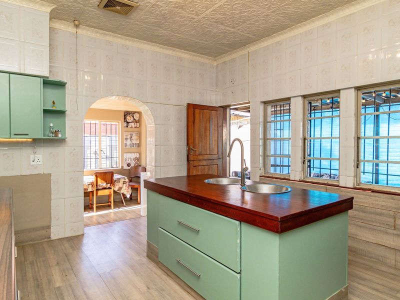 A dated kitchen featuring a central island with a double sink, light green cabinetry, tiled walls, and a textured ceiling with an arched doorway.