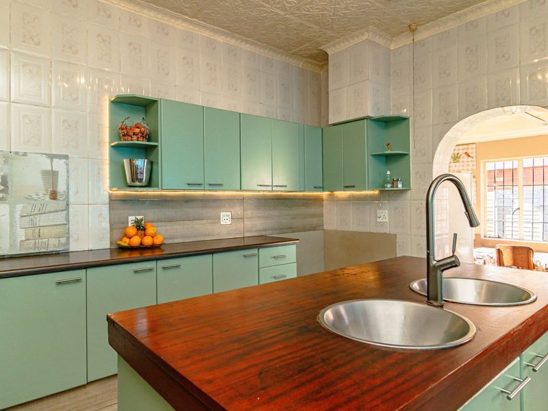 A kitchen featuring mint green cabinetry, a wooden island with a double stainless steel sink, and decorative tiled walls.