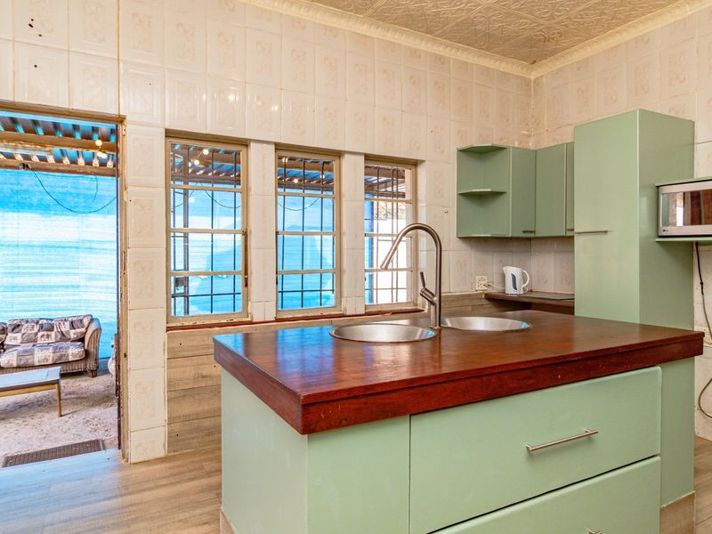 A dated kitchen featuring light green cabinetry, a wooden countertop with a double sink, and tiled wall finishes, offering potential for modernization.
