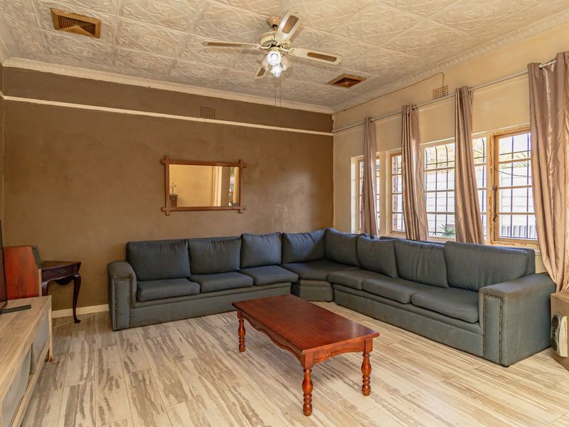 A living room featuring a traditional pressed metal ceiling, ceiling fan, and tiled flooring, with security bars installed on the windows.