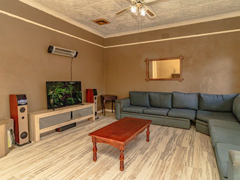 A living room featuring a decorative pressed metal ceiling, ceiling fan, wall-mounted heater, and tiled flooring.