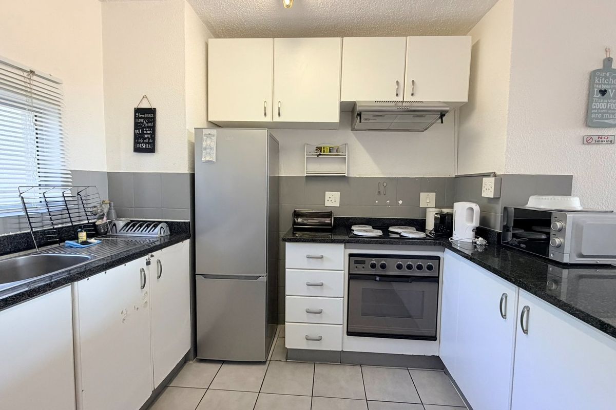 A functional kitchen featuring granite countertops, built-in cabinetry, a stainless steel sink, and integrated cooking appliances with a tiled backsplash.
