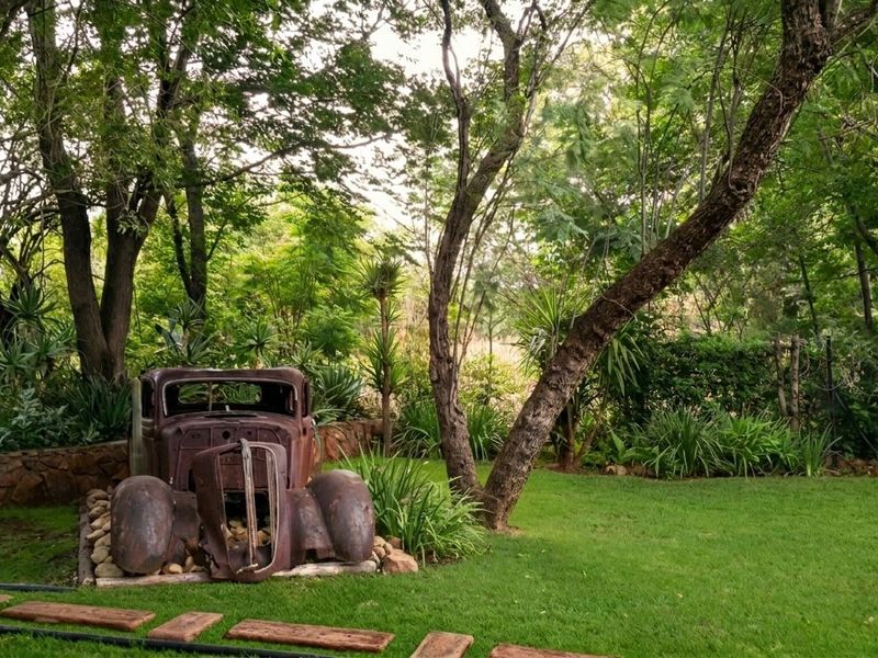 A lush, well-maintained garden area featuring mature trees, a stone retaining wall, and a manicured lawn.