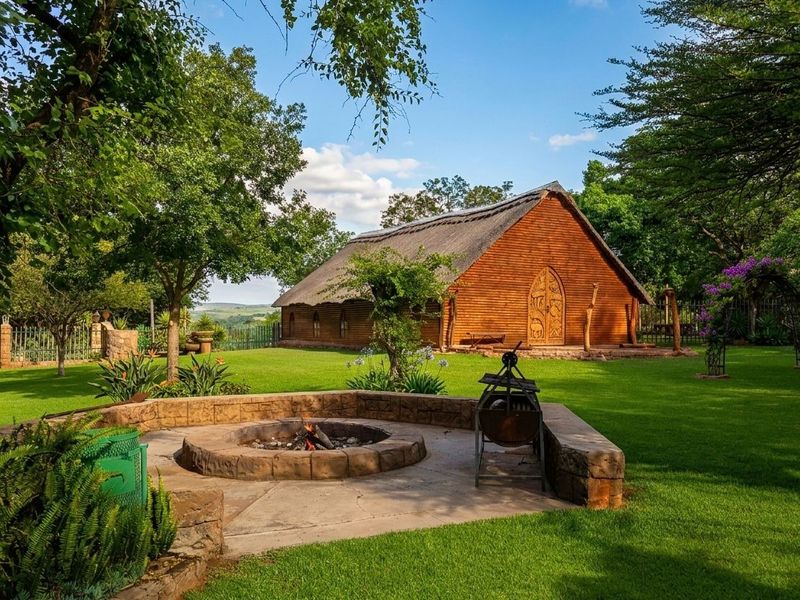 A beautifully landscaped garden featuring a stone fire pit area and a charming timber-clad building with a traditional thatched roof.
