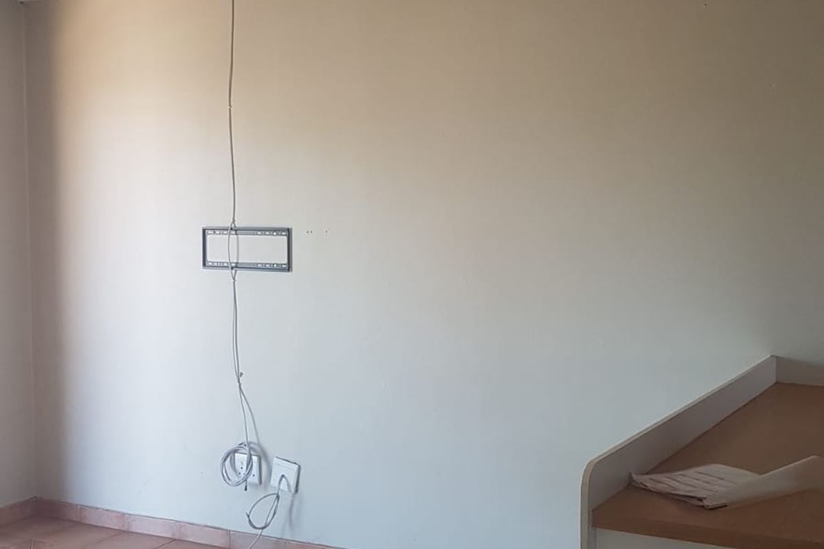 An empty living area featuring tiled flooring and a wall-mounted television bracket with exposed wiring, offering a blank canvas for potential updates.