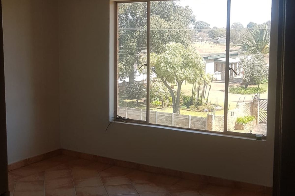 An empty bedroom featuring tiled flooring, a large window with natural light, and a ceiling-mounted spotlight fixture.