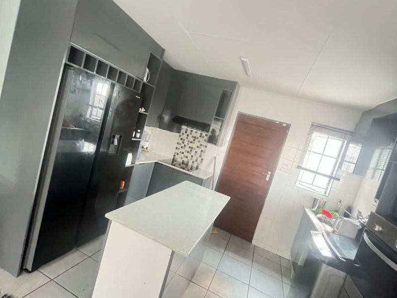 Modern kitchen featuring dark grey cabinetry, a central island, tiled flooring, and a mosaic backsplash with integrated oven and extractor fan.
