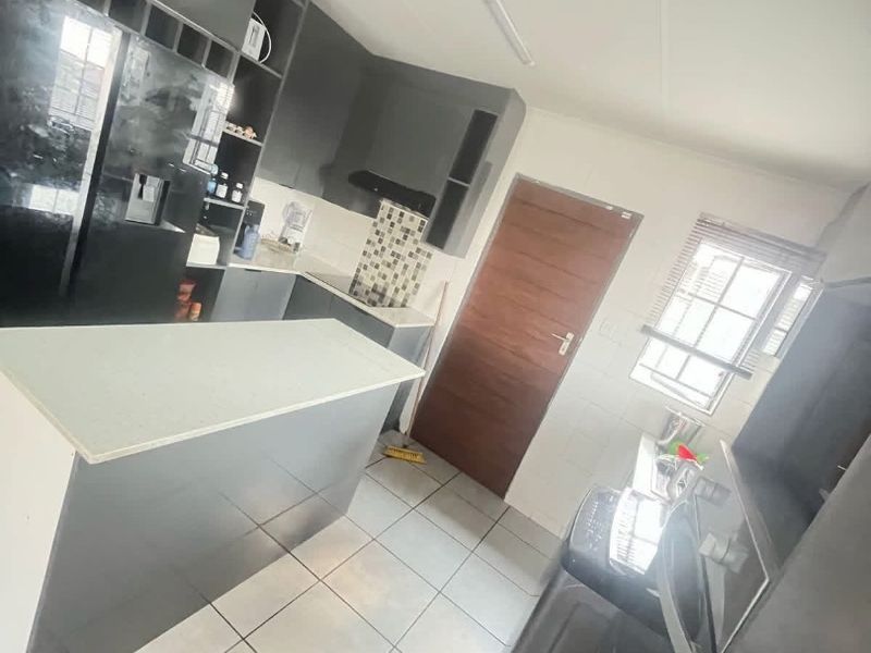 Modern kitchen featuring dark cabinetry, a central island, mosaic tile backsplash, and tiled flooring with direct access to an adjacent room.