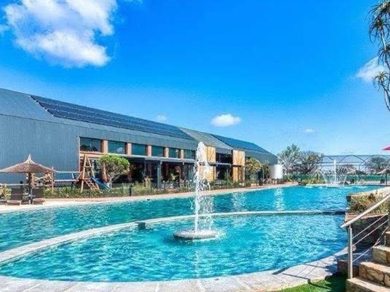 A well-maintained outdoor swimming pool area featuring a central water fountain, stone steps, and a large building with integrated solar panels.
