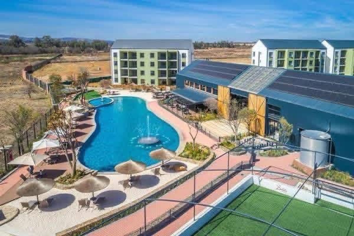 Aerial view of a modern apartment complex featuring a large swimming pool, landscaped grounds, solar-equipped clubhouse, and recreational sports facilities.