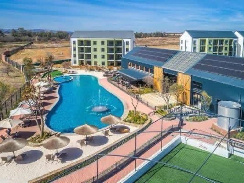 Aerial view of a modern apartment complex featuring a large swimming pool, landscaped grounds, solar-equipped clubhouse, and recreational sports facilities.